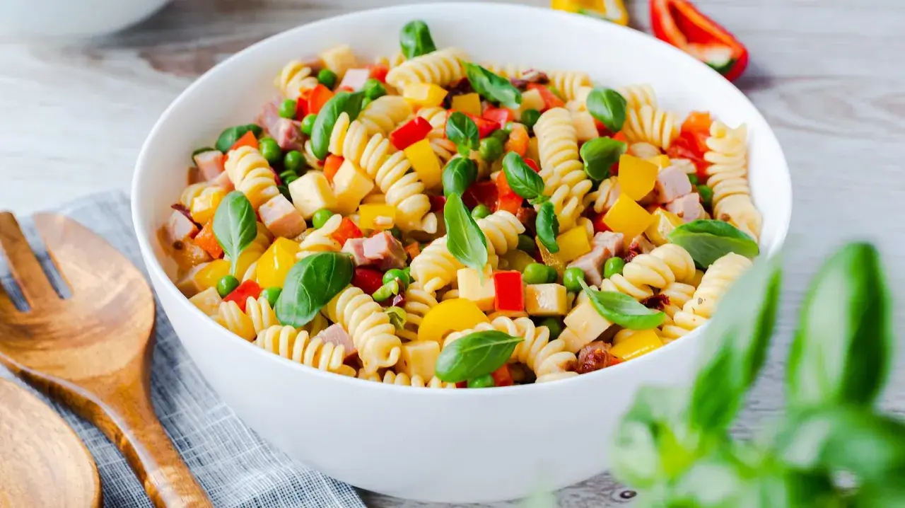 Bester Pasta Salat ohne Mayonnaise: Spiralnudeln mit Schinken, Erbsen, Paprika und Basilikum in einer weißen Schüssel.