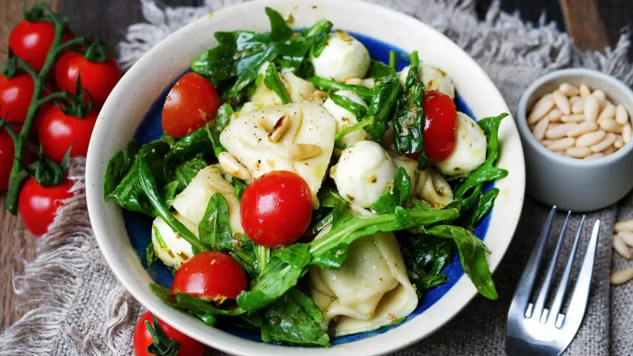 Ein köstlicher tortellini salat mit pesto, garniert mit Kirschtomaten, Mozzarella-Kugeln und Pinienkernen.