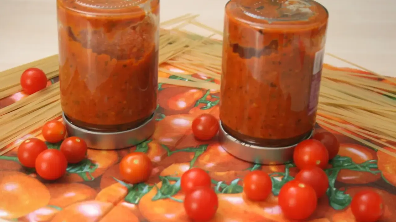 Zwei Gläser mit Tomatensoße, umgeben von frischen Tomaten und Spaghetti. Perfekt für die Tomaten haltbar machen.