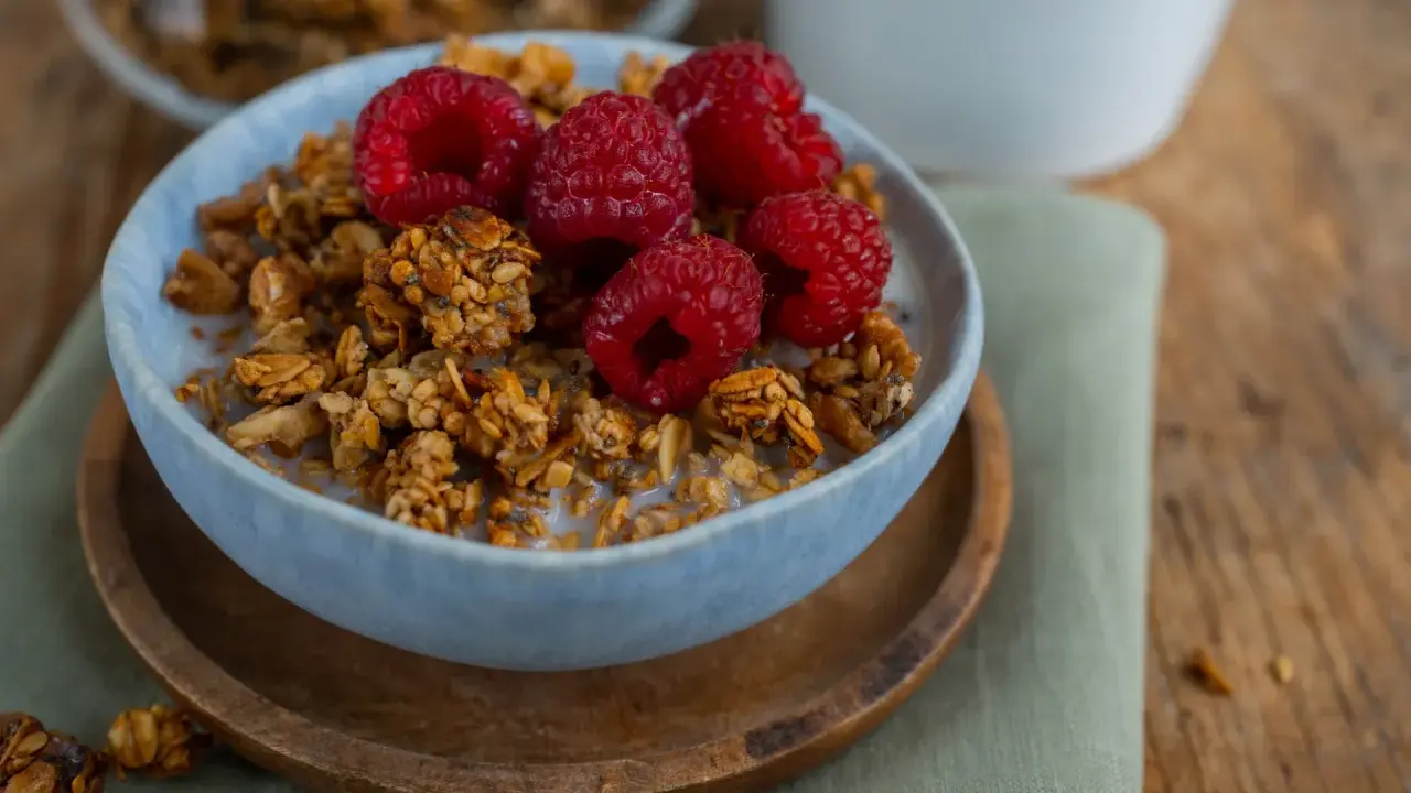 Schüssel mit selbstgemachtem Granola, Milch und frischen Himbeeren. Ein gesunder Start in den Tag!