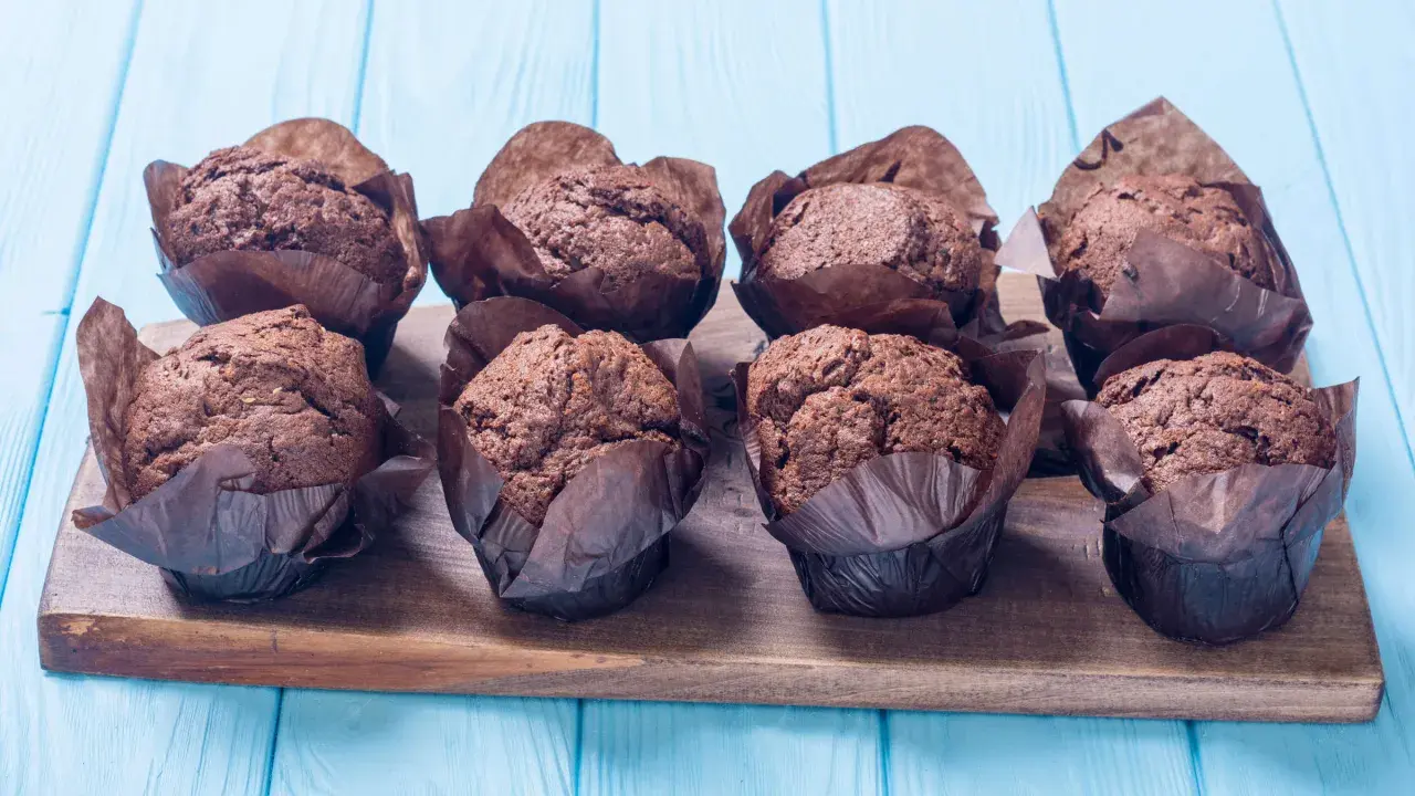 Acht schokoladige Muffins im braunen Papier auf einem Holzbrett. Perfekt für ein schokomuffins rezept.