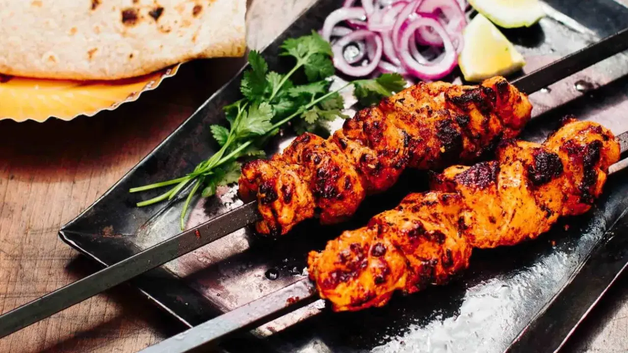 Zwei Spieße mit saftigem Tandoori Chicken, garniert mit Koriander, Zwiebelringen und Zitronenspalten. Dazu Fladenbrot.