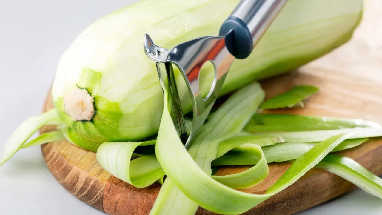 Zucchini wird geschält, aber man kann Zucchini mit Schale essen. Die grünen Streifen der Schale liegen auf dem Holzbrett.