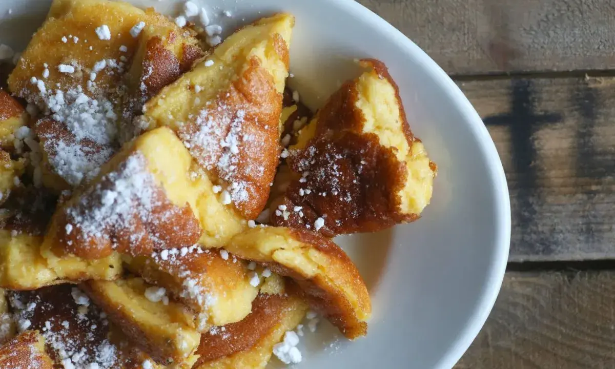 Ein Teller mit goldbraunem Kaiserschmarrn, bestäubt mit Puderzucker. Dieses Kaiserschmarrn Rezept ist ein Genuss!