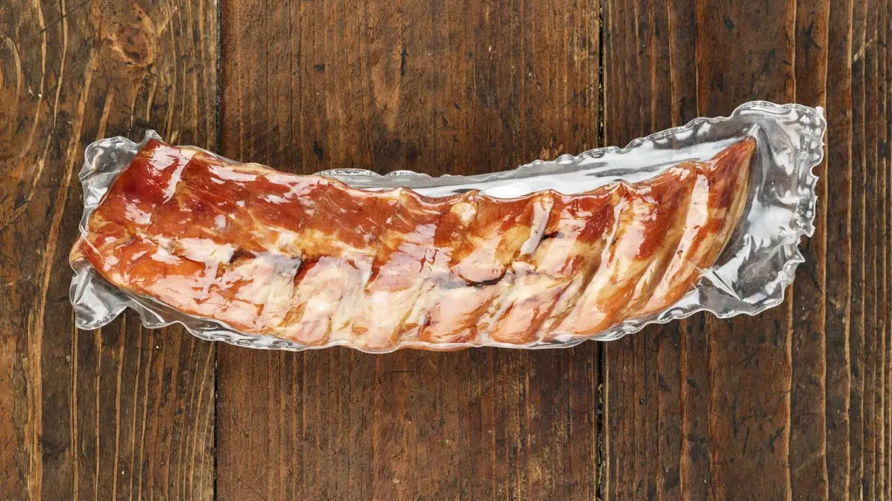 Vakuumverpackte Spareribs sous vide, bereit für die Zubereitung, liegen auf einer rustikalen Holzoberfläche.