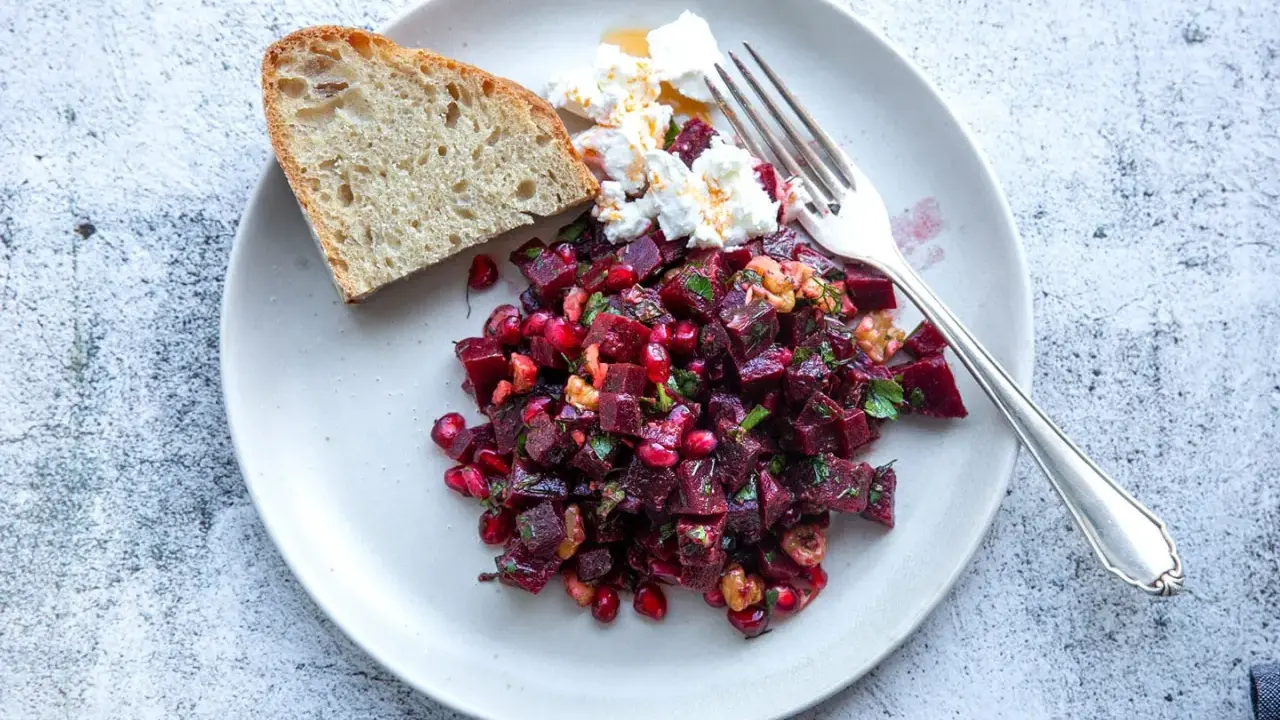 Ein bunter rote beete salat mit Granatapfelkernen, Nüssen und Ziegenkäse, serviert mit Brot.