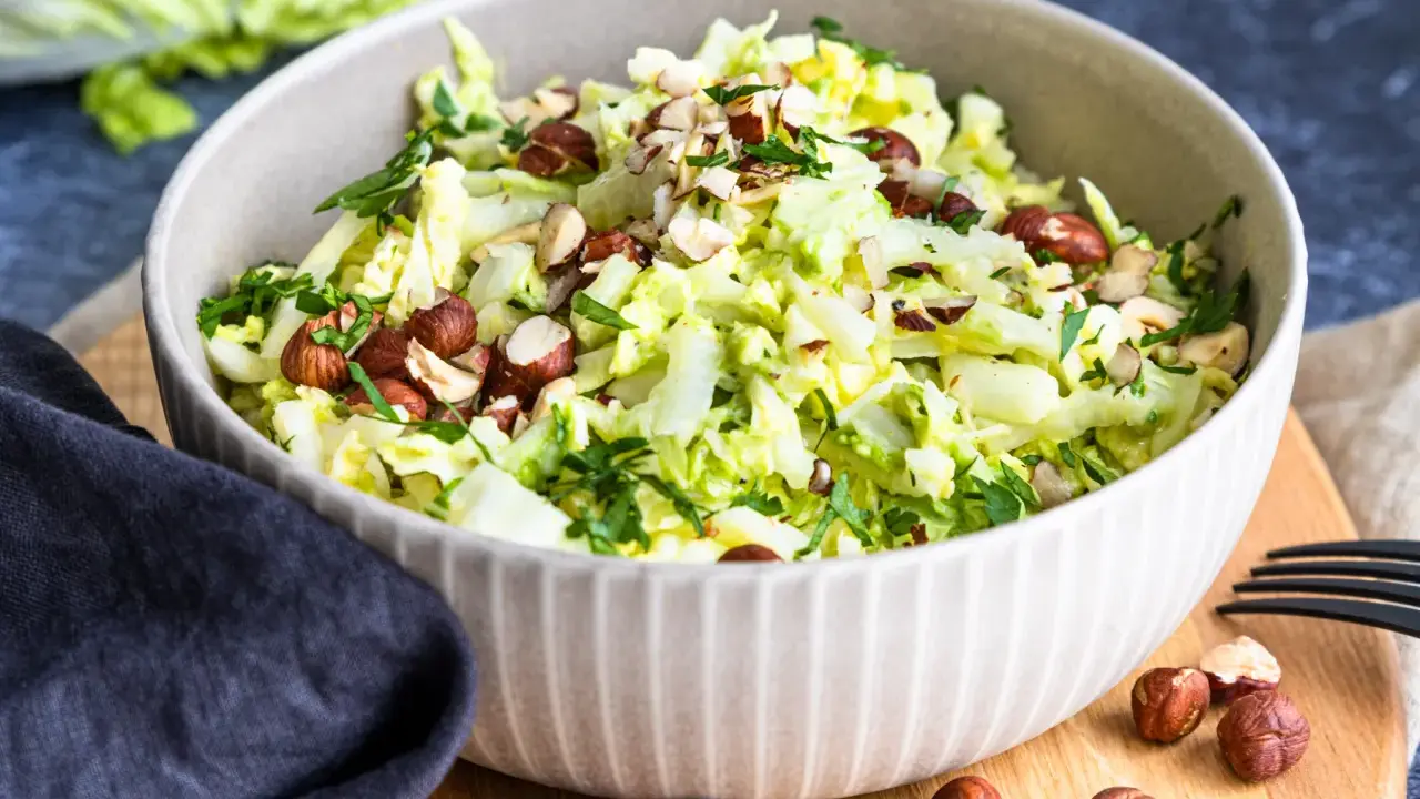 Frischer Chinakohlsalat mit gehackten Haselnüssen und Petersilie, garniert mit ganzen Nüssen.