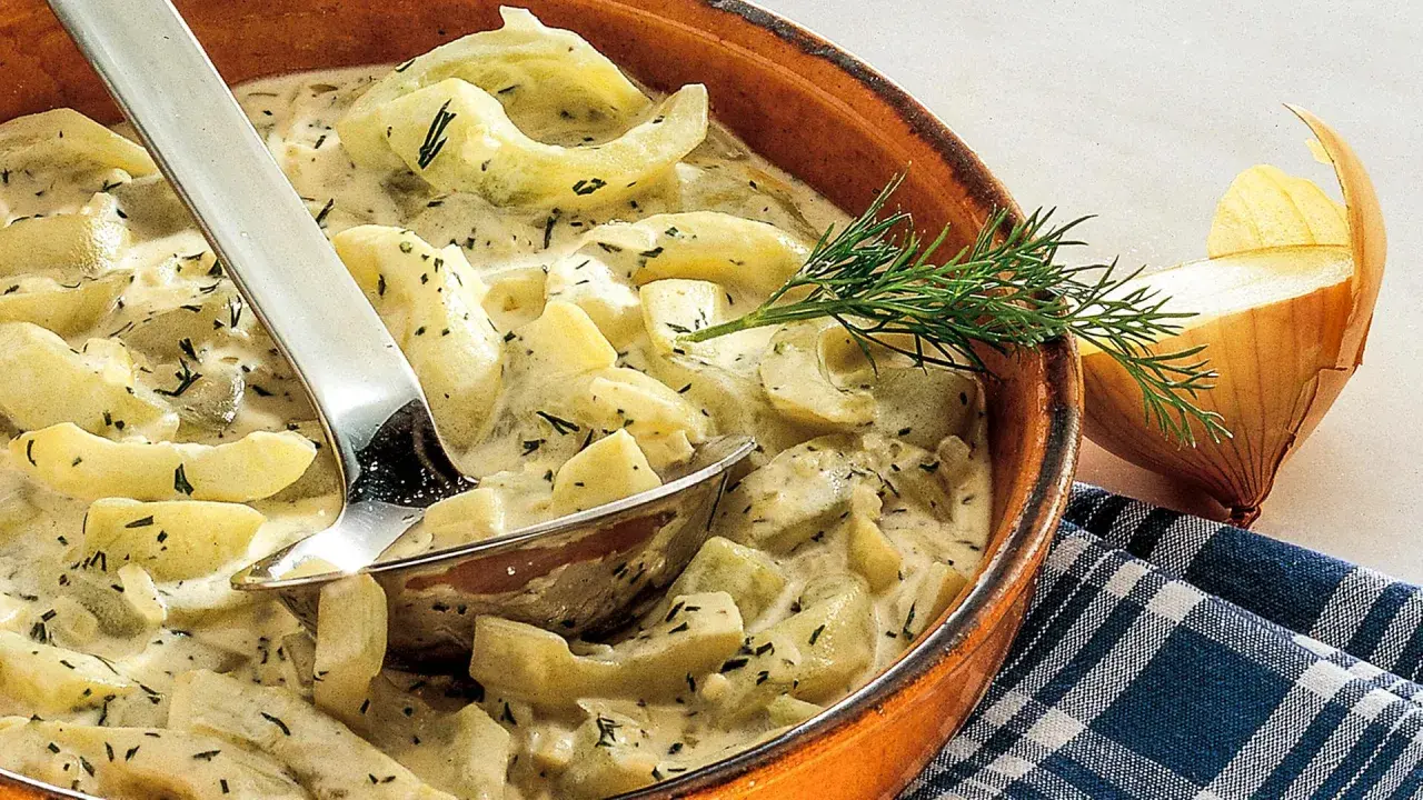 Schmorgurken in cremiger Soße mit Dill, daneben eine Zwiebel. So sehen sie aus, lecker und appetitlich.