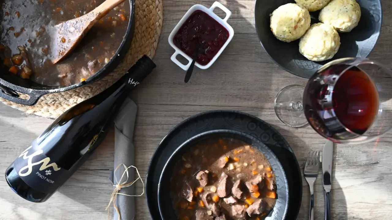 Herzhaftes Wild im Dutch Oven, serviert mit Klößen, Preiselbeeren und einem Glas Rotwein. Ein Festmahl!