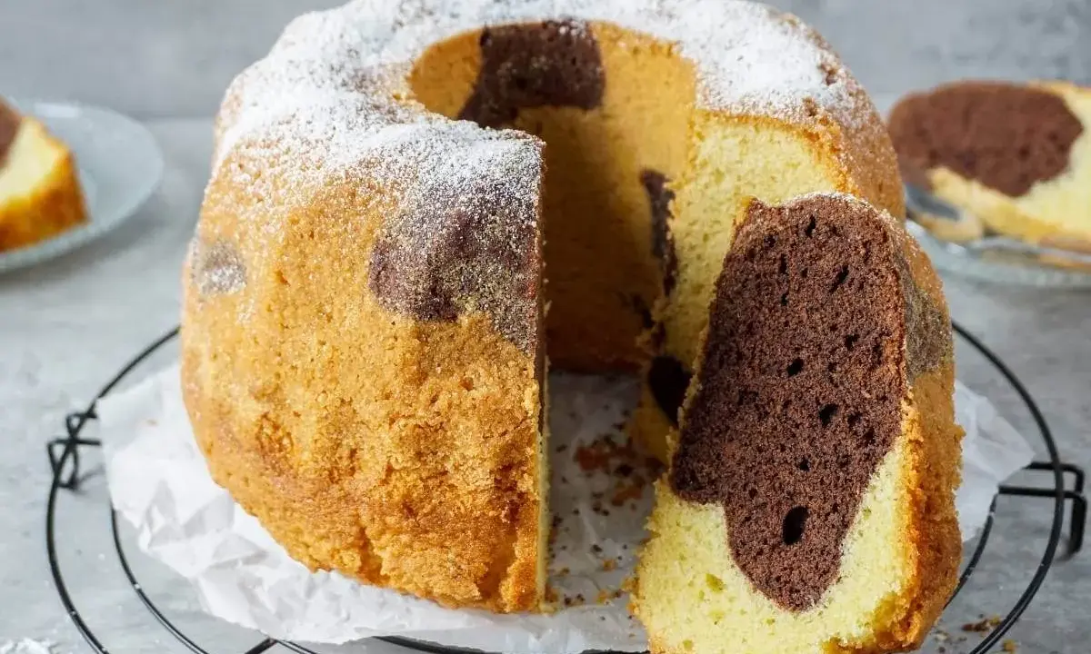 Ein saftiger Marmorkuchen mit Puderzucker bestäubt, ein Stück abgetrennt, das die schöne Marmorierung zeigt.