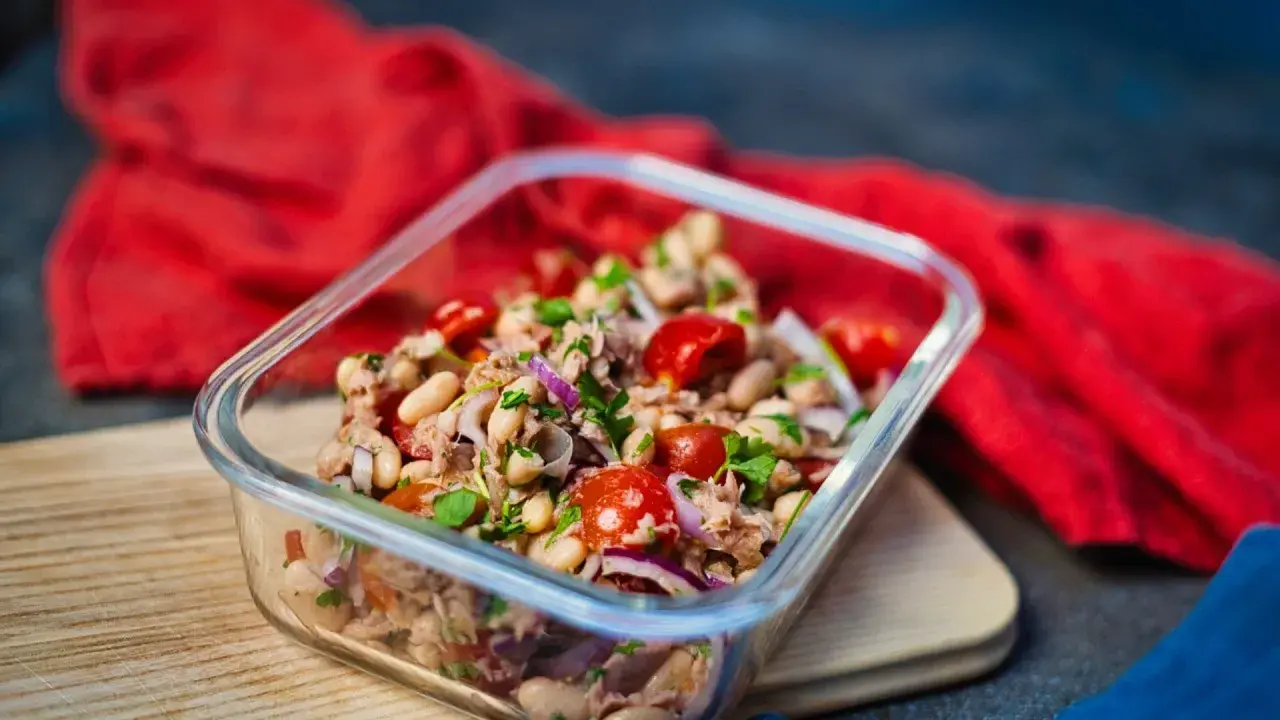 Frischer Thunfischsalat mit weißen Bohnen, Tomaten und roten Zwiebeln in einer Glasbox, bereit zum Mitnehmen.