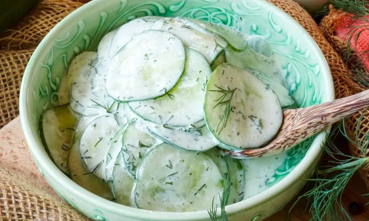 Frischer gurkensalat mit saurer sahne und dill, serviert in einer grünen schüssel.