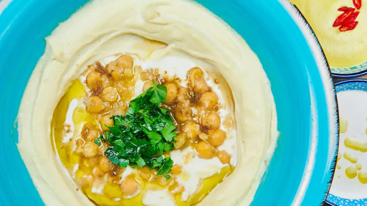 Cremiger Hummus, garniert mit Kichererbsen, Petersilie und Olivenöl. Ein authentisches Hummus Rezept original arabisch, serviert in einer blauen Schüssel.