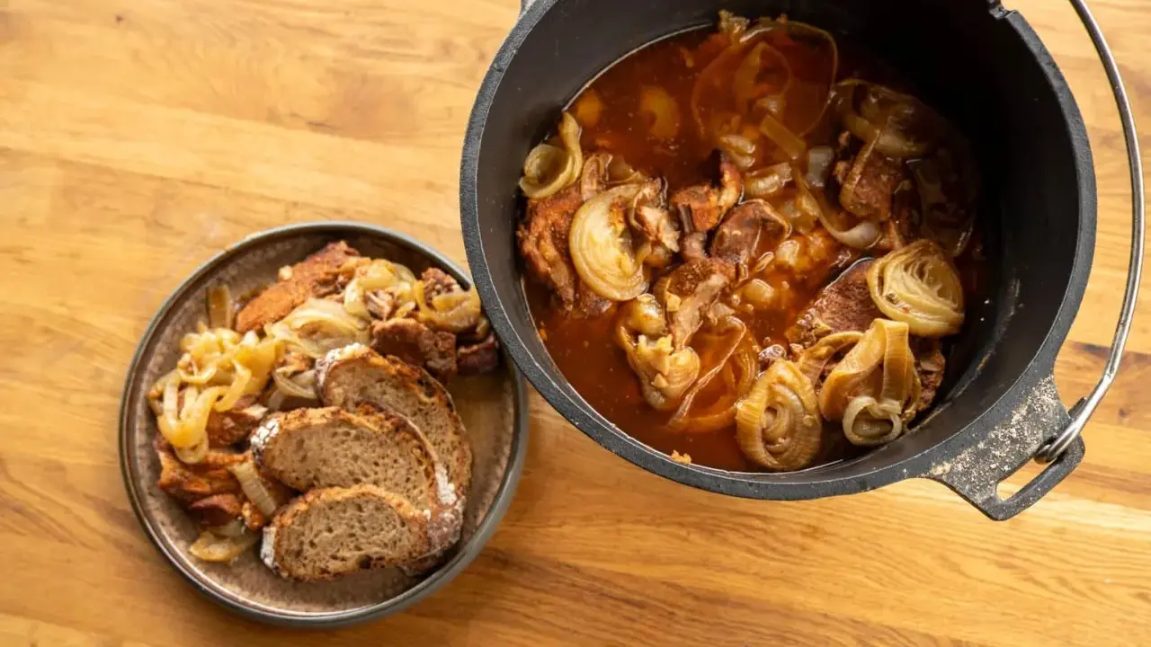 Herzhaftes Zwiebelfleisch im Dutch Oven, daneben eine Portion mit Brot auf einem Teller.