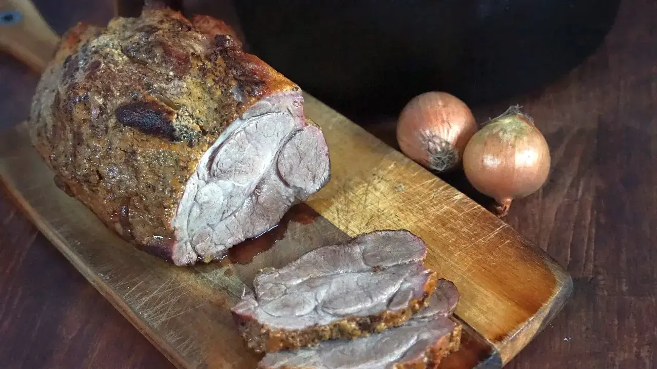 Saftiger Rinderbraten aus dem Dutch Oven, auf einem Holzbrett mit Zwiebeln.