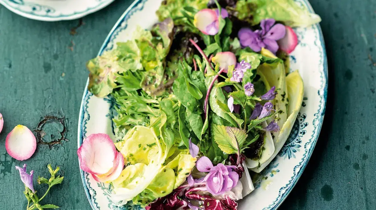 Ein bunter gemischter Salat mit zarten Blüten und Radieschen auf einem verzierten Teller.