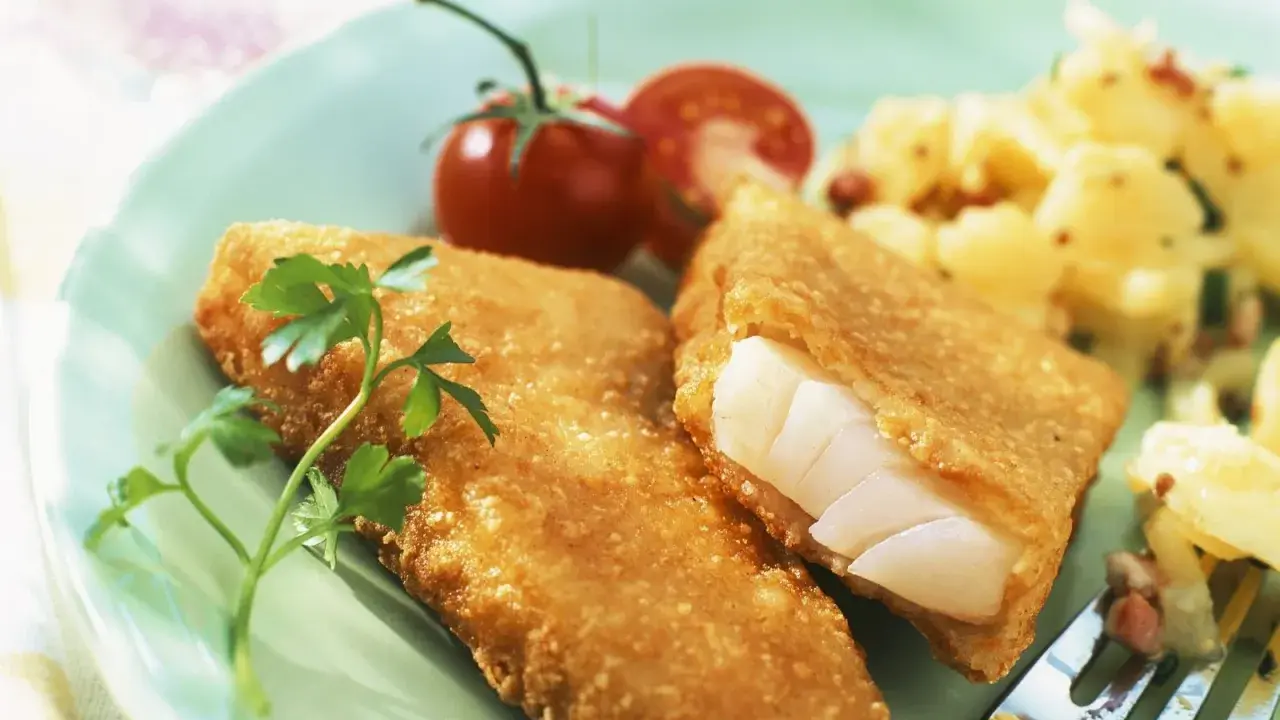 Knuspriger Backfisch mit cremigem Kartoffelsalat und frischer Petersilie, garniert mit Kirschtomaten.