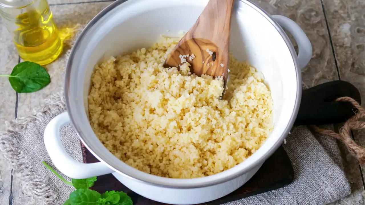 Frisch zubereiteter Couscous als Beilage in einem Topf, daneben ein Glas Öl und Minzblätter.