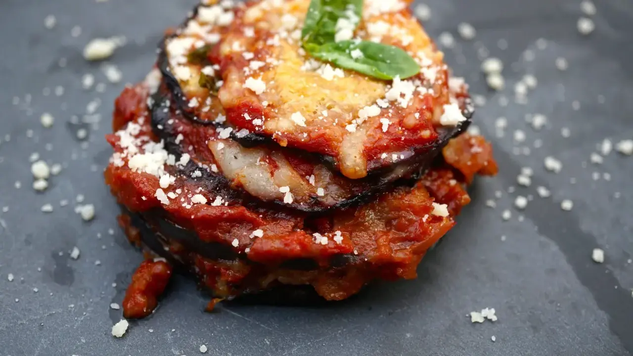 Melanzane alla Parmigiana: geschichtete Aubergine mit Tomatensauce, Käse und Basilikum, bestreut mit Parmesan.
