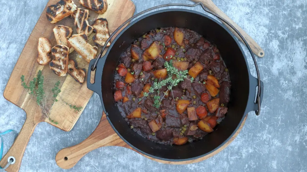 Herzhaftes Rindfleischgulasch im Dutch Oven, mit Kartoffeln, Karotten und Erbsen. Dazu geröstetes Brot. Perfekt für Dutch Oven Rezepte Rind.