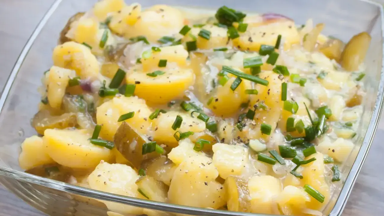 Kartoffelsalat ohne Mayo, mit Gurken, Zwiebeln und Schnittlauch in einer Glasschüssel.
