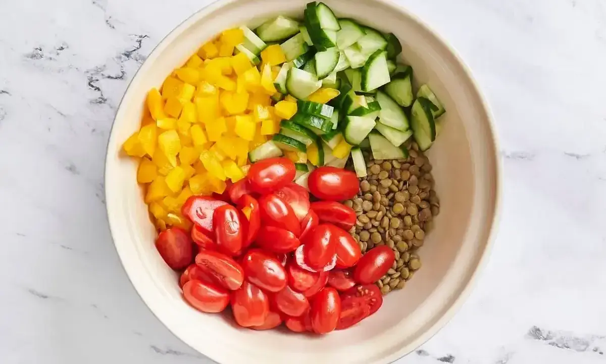 Zutaten für ein Linsensalat Rezept: gekochte Linsen, gewürfelte gelbe Paprika, Kirschtomaten und Gurkenstücke in einer Schüssel.