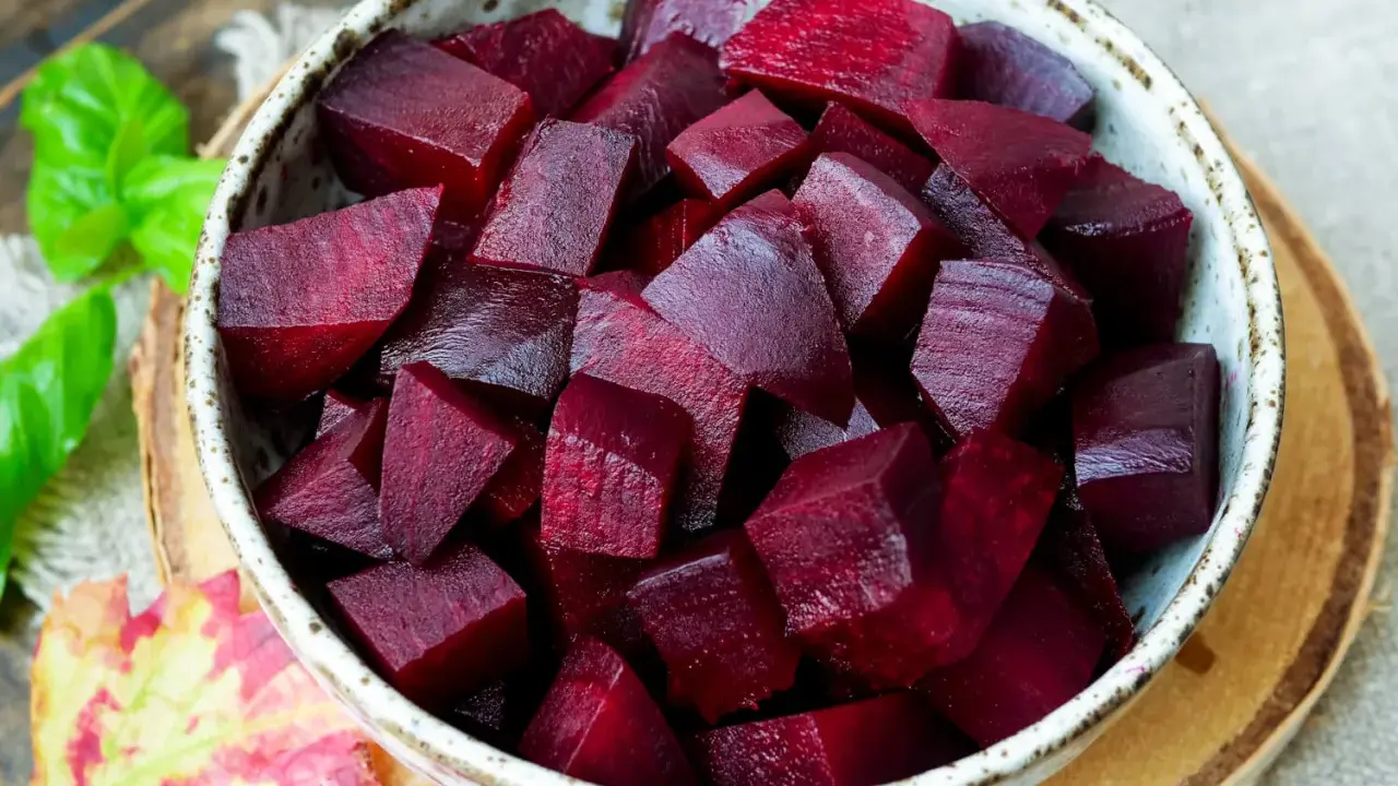Schüssel mit gewürfelter roter Bete, bereit für die Kochzeit. Frische grüne Blätter und ein Herbstblatt liegen daneben.