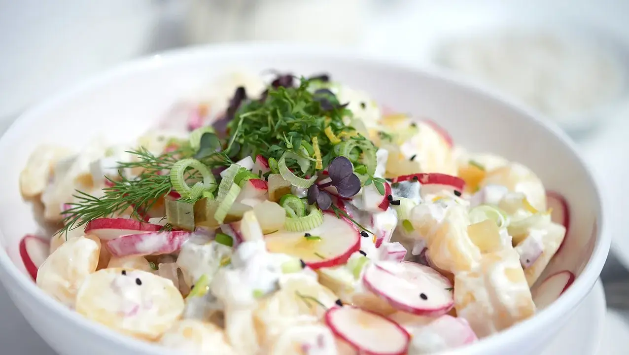 Ein cremiger Kartoffel Radieschen Salat, garniert mit frischen Kräutern und Frühlingszwiebeln.
