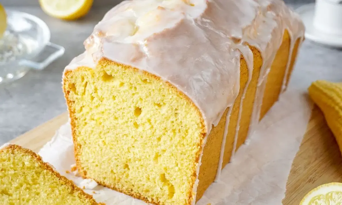 Saftiger Zitronenkuchen mit Zuckerguss, der aussieht wie der beste zitronenkuchen der welt. Ein Stück ist bereits angeschnitten.