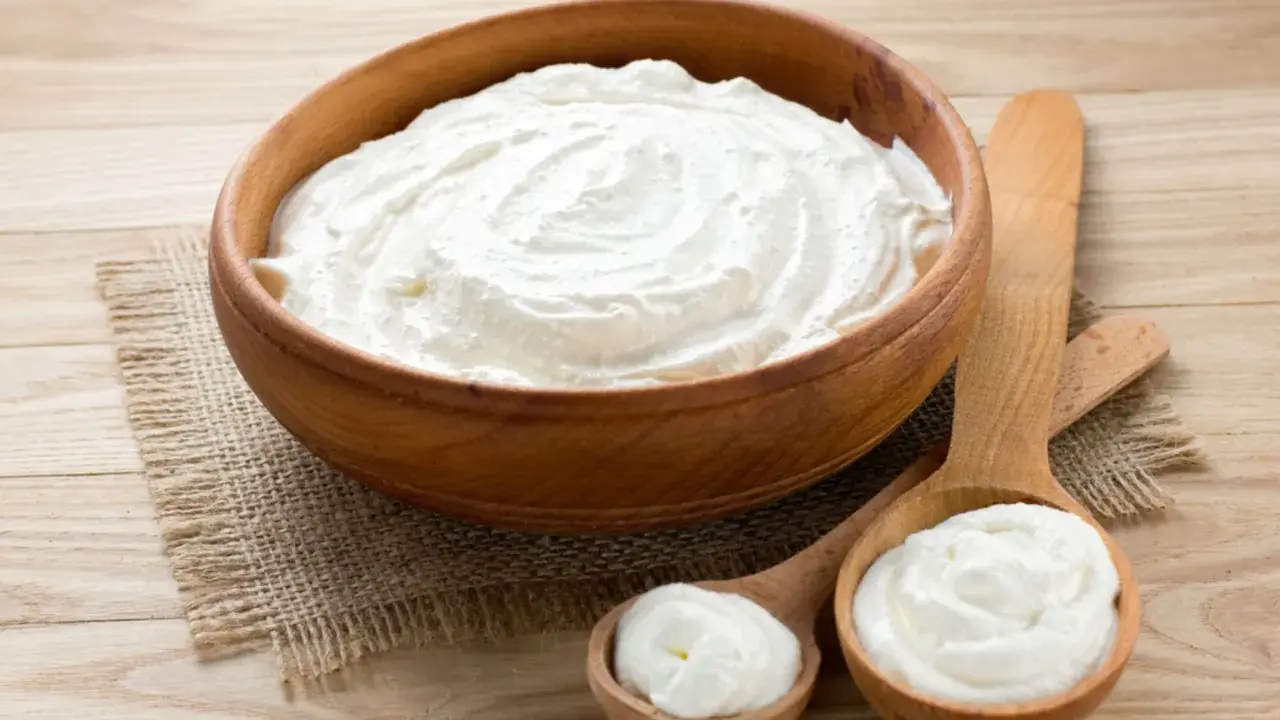 Cremiger Schmand in Holzschale und Löffeln. Ist Schmand gesund? Ja, in Maßen genossen, liefert er Kalzium und Proteine.