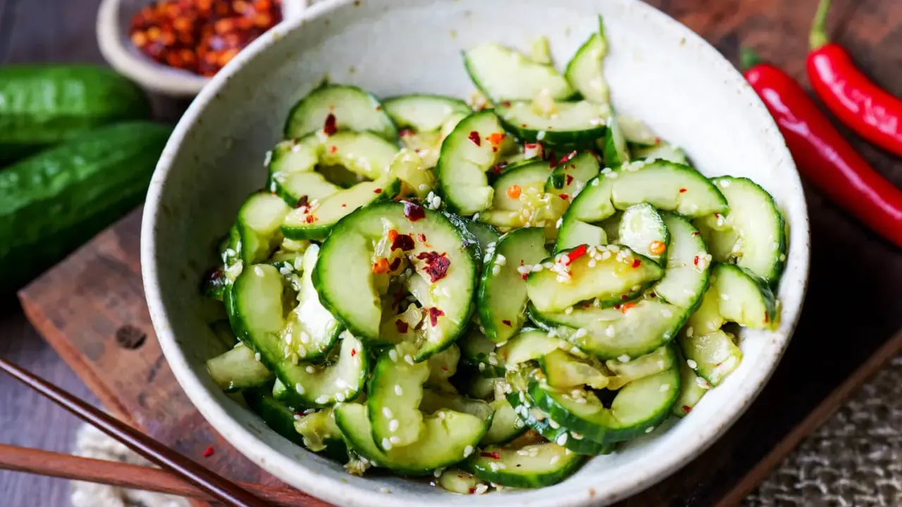 Erfrischender asiatischer Gurkensalat mit Sesam und Chili-Flocken, serviert in einer Schale mit Essstäbchen.