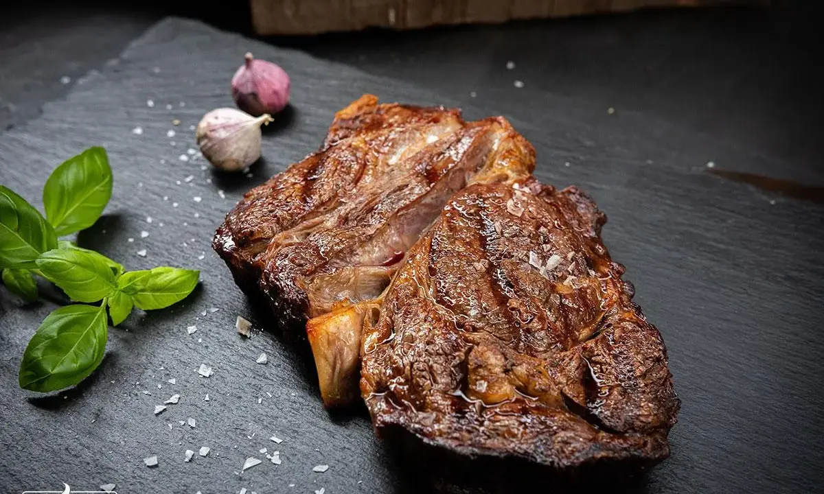 Perfekt gegrilltes Rib Eye Steak mit grobem Salz, Basilikum und Knoblauch auf schwarzem Stein.
