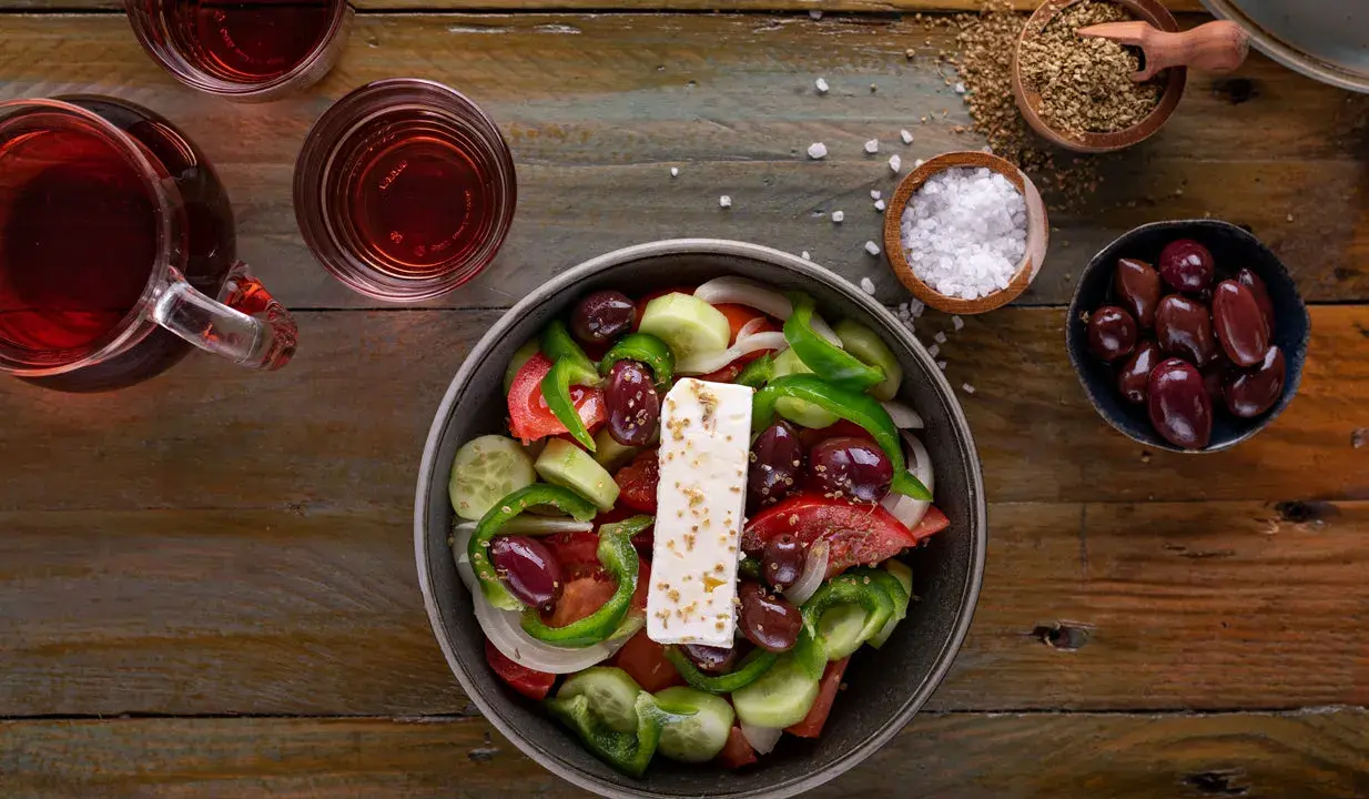 Frischer griechischer Salat mit Feta, Oliven, Tomaten, Gurken und Paprika, serviert mit Rotwein und Gewürzen.