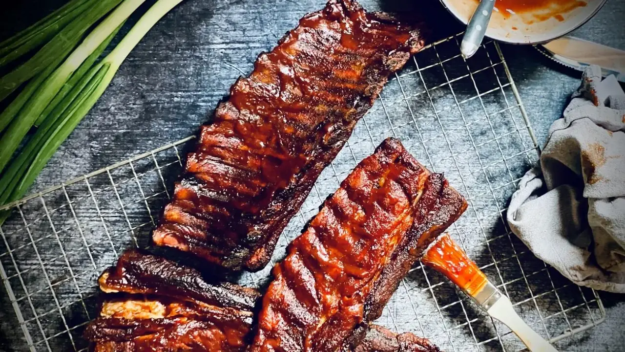 Saftige spareribs grillen holzkohle, mit BBQ-Sauce bestrichen, bereit zum Genuss. Grüne Frühlingszwiebeln und ein Pinsel liegen daneben.
