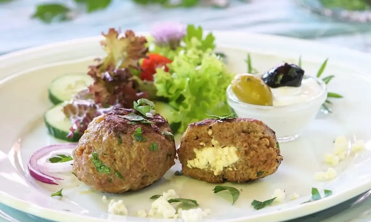 Gefüllte Bifteki mit Feta, serviert mit Salat, Gurken, Zwiebeln und Tzatziki. Ein köstliches Bifteki Rezept für Genießer.