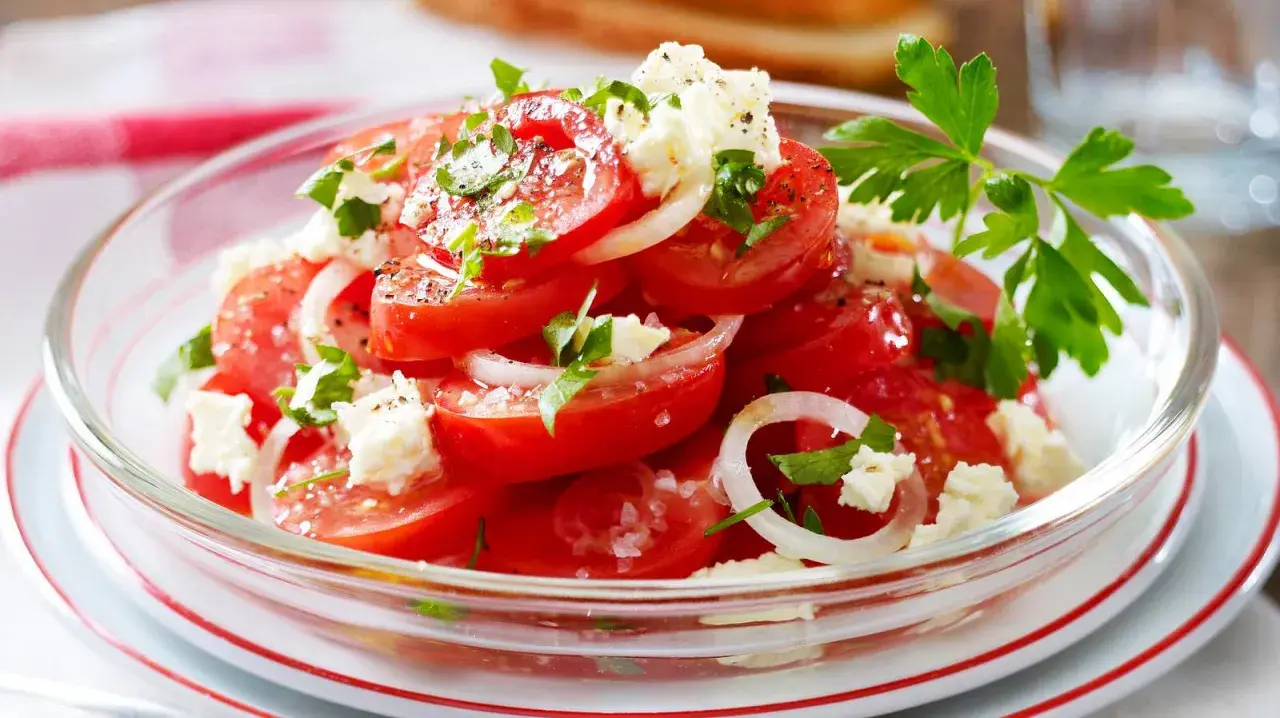 Frischer Tomatensalat mit Feta, Zwiebeln und Petersilie, garniert mit grobem Salz und Pfeffer. Ein leichter Genuss!