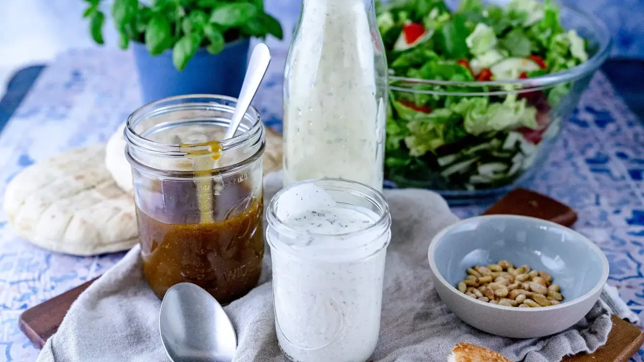 Ein Glas cremiges **ranch dressing** steht neben einem Glas mit brauner Soße, einem Salat und Brot.