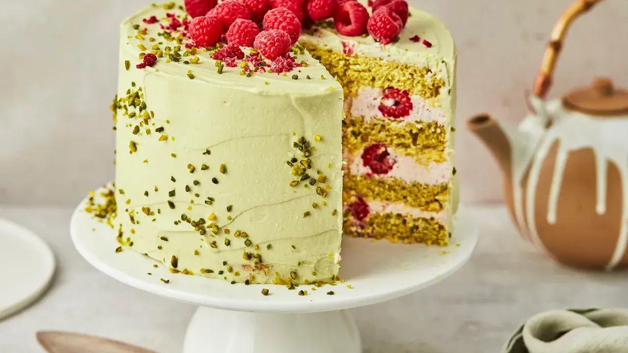 Himbeer Pistazien Torte mit frischen Beeren und knackigen Pistazien. Ein Stück ist angeschnitten und zeigt die saftige Füllung.