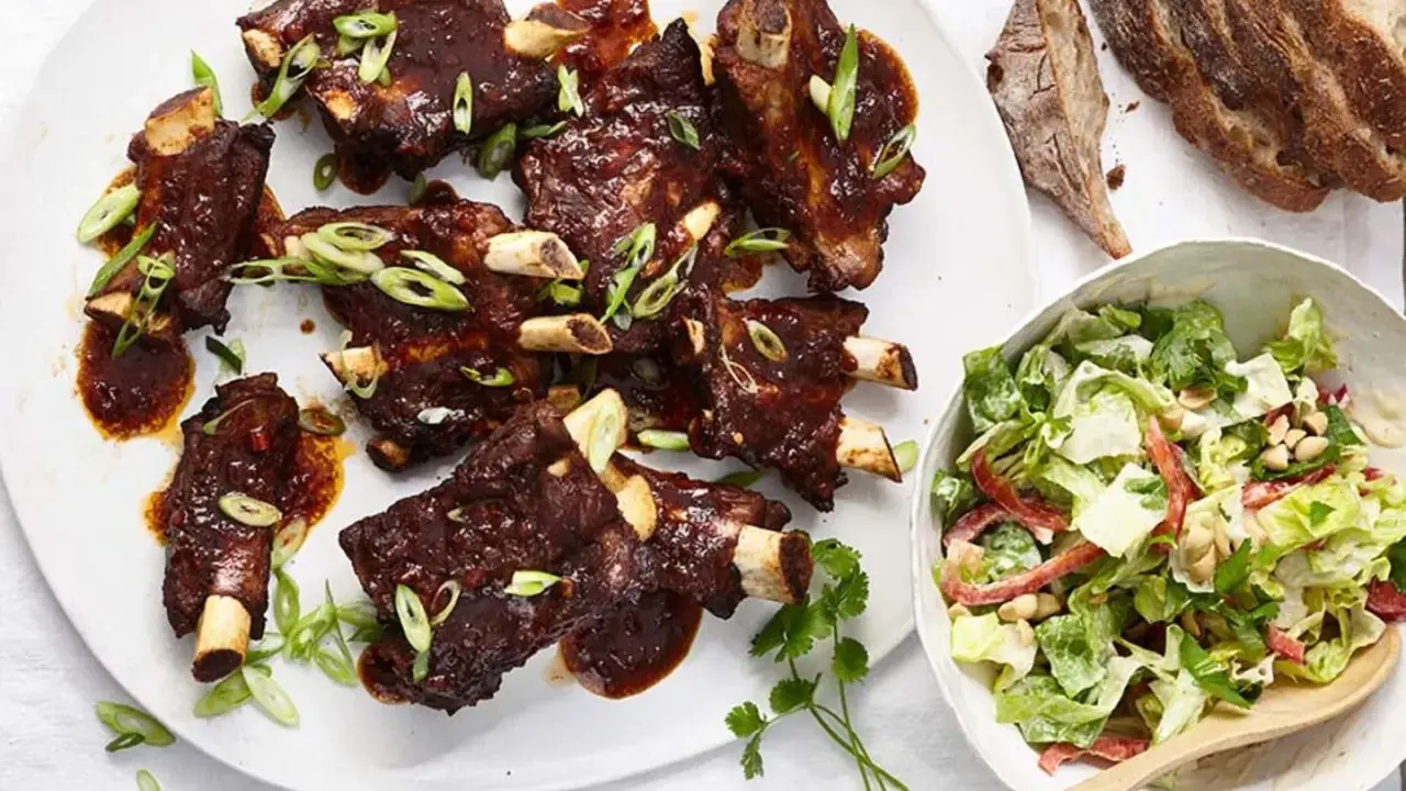 Saftige Spareribs mit BBQ-Sauce und Frühlingszwiebeln, serviert mit einem frischen Salat.