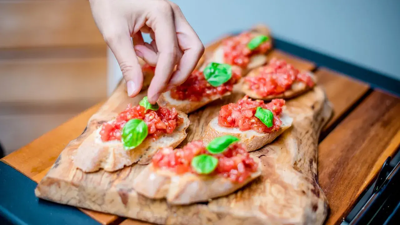 Frische Bruschetta vom Grill, belegt mit Tomaten und Basilikum, wird von einer Hand garniert.