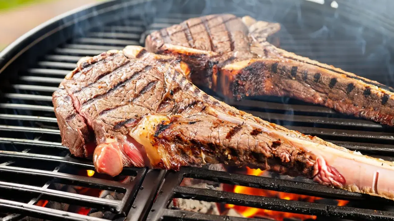 Zwei saftige tomahawk steaks brutzeln auf dem Grill. Rauch steigt auf, die Kohlen glühen.