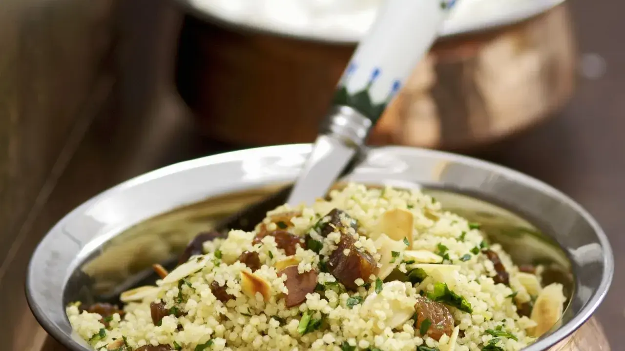 Ein köstlicher Couscous mit Rosinen, Mandelsplittern und frischer Petersilie, serviert in einer Kupferschale.