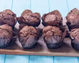 Acht schokoladige Muffins im braunen Papier auf einem Holzbrett. Perfekt für ein schokomuffins rezept.
