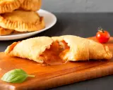 Leckeres Panzerotti-Rezept im Ofen, gefüllt mit Tomaten und Käse. Ein goldbrauner Teig, der auf einer Holzplatte mit Basilikum und Kirschtomate serviert wird.