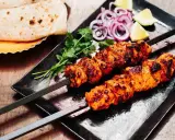 Zwei Spieße mit saftigem Tandoori Chicken, garniert mit Koriander, Zwiebelringen und Zitronenspalten. Dazu Fladenbrot.
