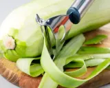 Zucchini wird geschält, aber man kann Zucchini mit Schale essen. Die grünen Streifen der Schale liegen auf dem Holzbrett.