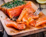 Frisch gebeizter Lachs mit Dill und Salz auf einem Holzbrett. Eine Gabel nimmt ein Stück Lachs auf.