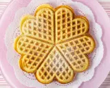Herzförmige Waffeln ohne Ei, bestäubt mit Puderzucker, auf einem rosa Teller mit Spitzendeckchen.