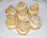 Windbeutel nach Omas Rezept, mit viel Sahne gefüllt und mit Puderzucker bestäubt, auf einem weißen Teller arrangiert.