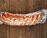Vakuumverpackte Spareribs sous vide, bereit für die Zubereitung, liegen auf einer rustikalen Holzoberfläche.